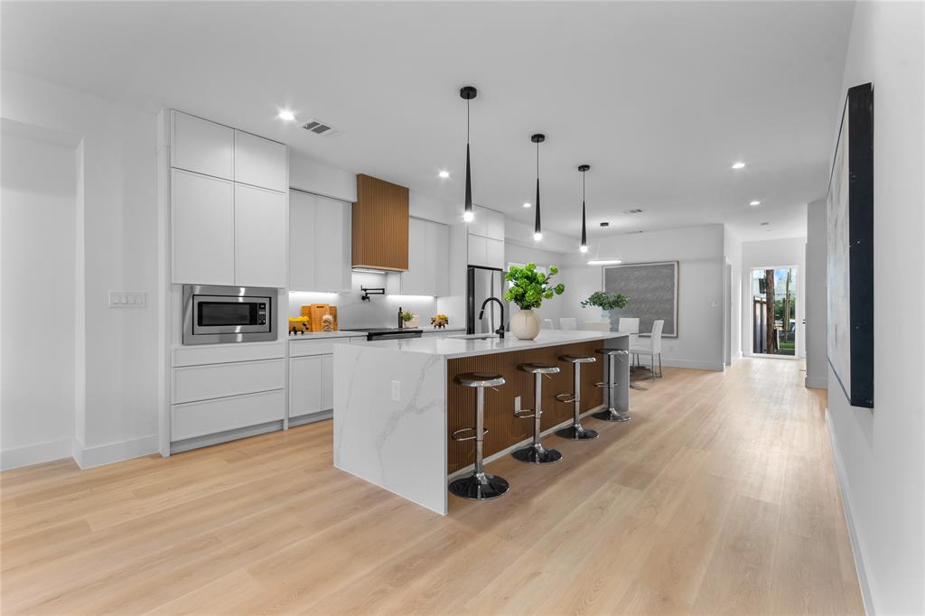 Gourmet kitchen featuring a waterfall island with integrated seating, stainless steel microwave, light wood-finish flooring, and pendant lighting