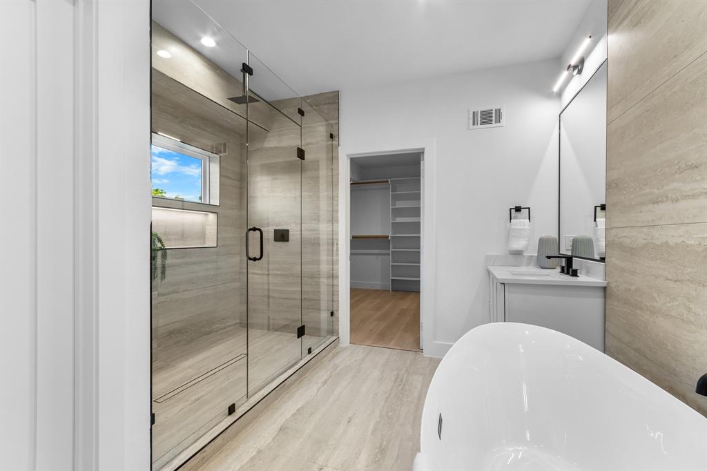 Spacious bathroom featuring a glass-enclosed shower with stone-look tile, integrated shelving, and a window