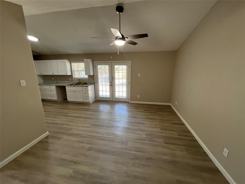 Vaulted ceiling with a ceiling fan, wood-finish flooring, white cabinetry, integrated sink, and double glass-paned doors