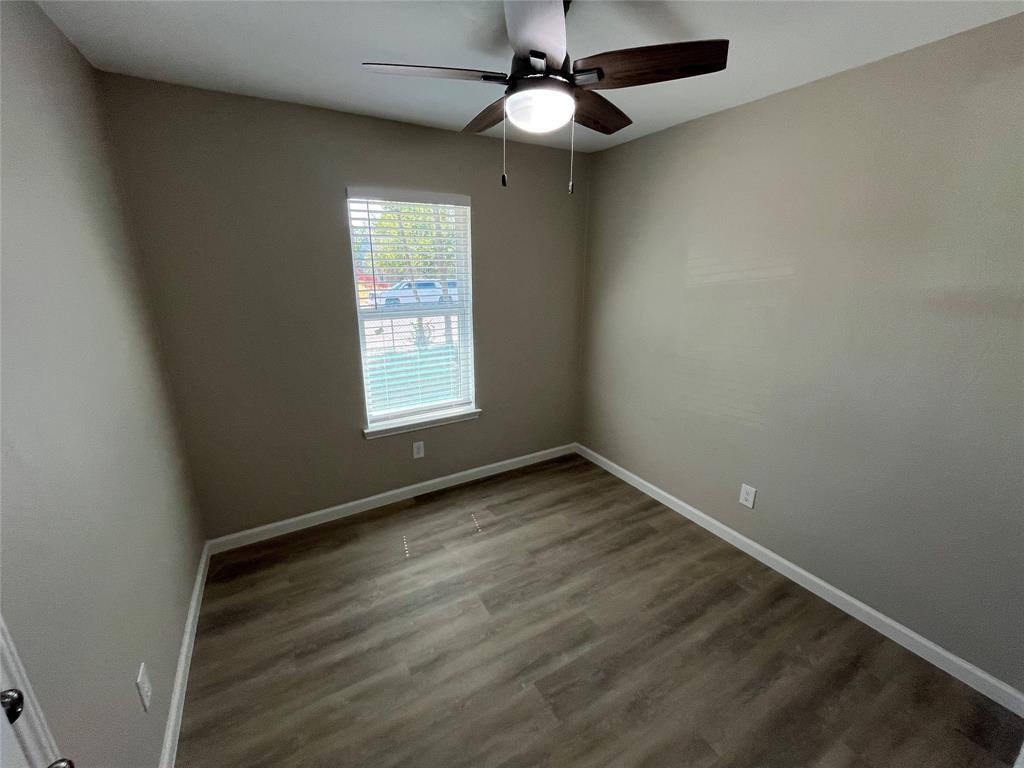 Wood-finish flooring, neutral wall tones, window with white blinds, and a ceiling fan with integrated lighting