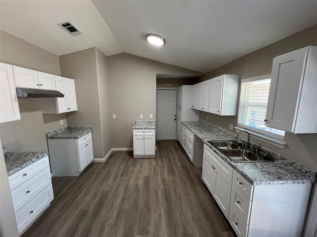 Spacious kitchen featuring white shaker cabinetry, granite-patterned countertops, wood-finish flooring, a double basin stainless steel sink, and a range hood