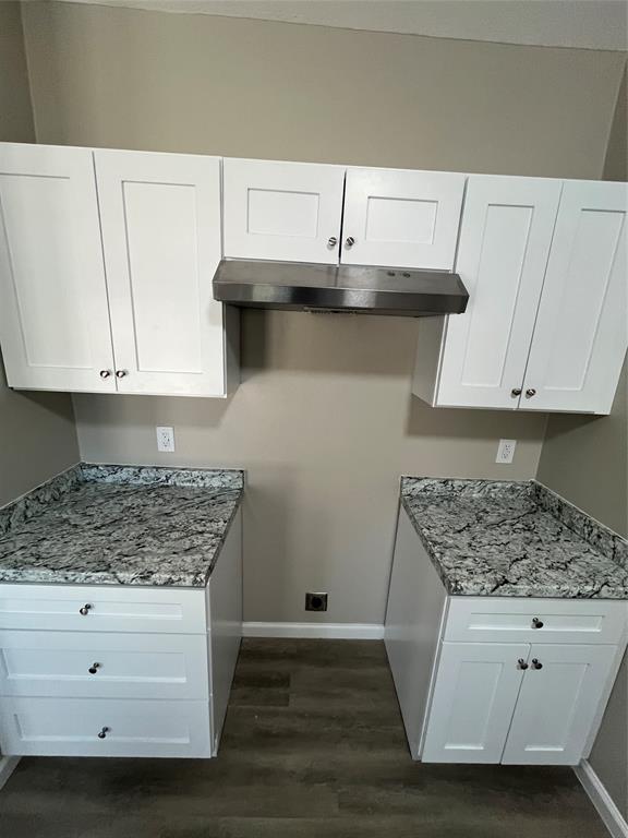 White shaker-style cabinetry, stainless steel range hood, stone-finish countertops, wood-finish flooring, and neutral wall paint