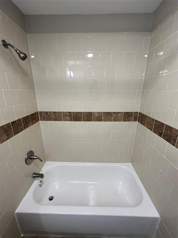 White subway tile surround with decorative accent band, white bathtub, and brushed nickel fixtures