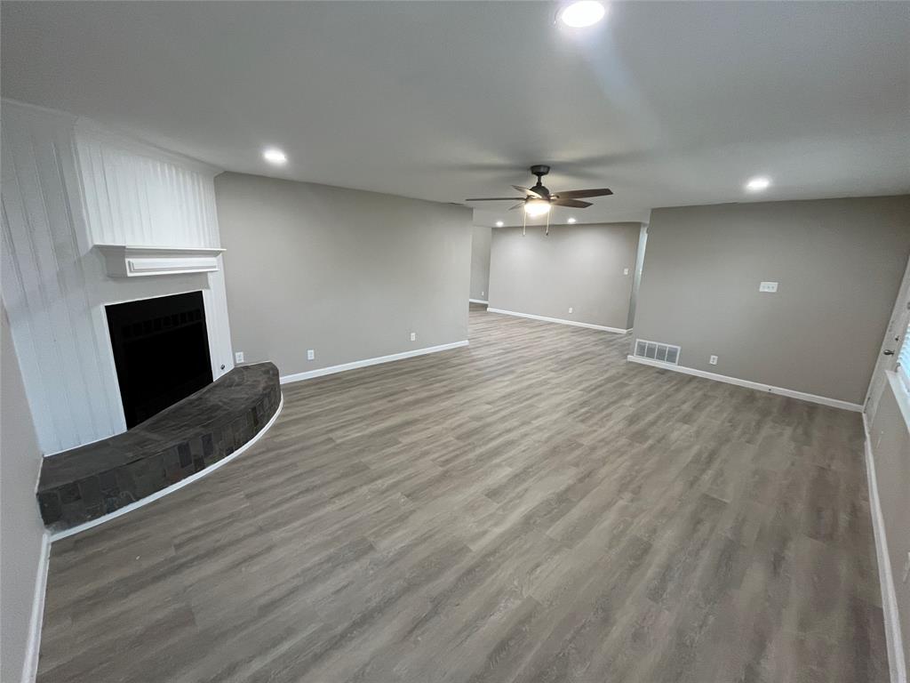 Spacious living area featuring wood-finish flooring, a fireplace with a stone hearth, and recessed lighting