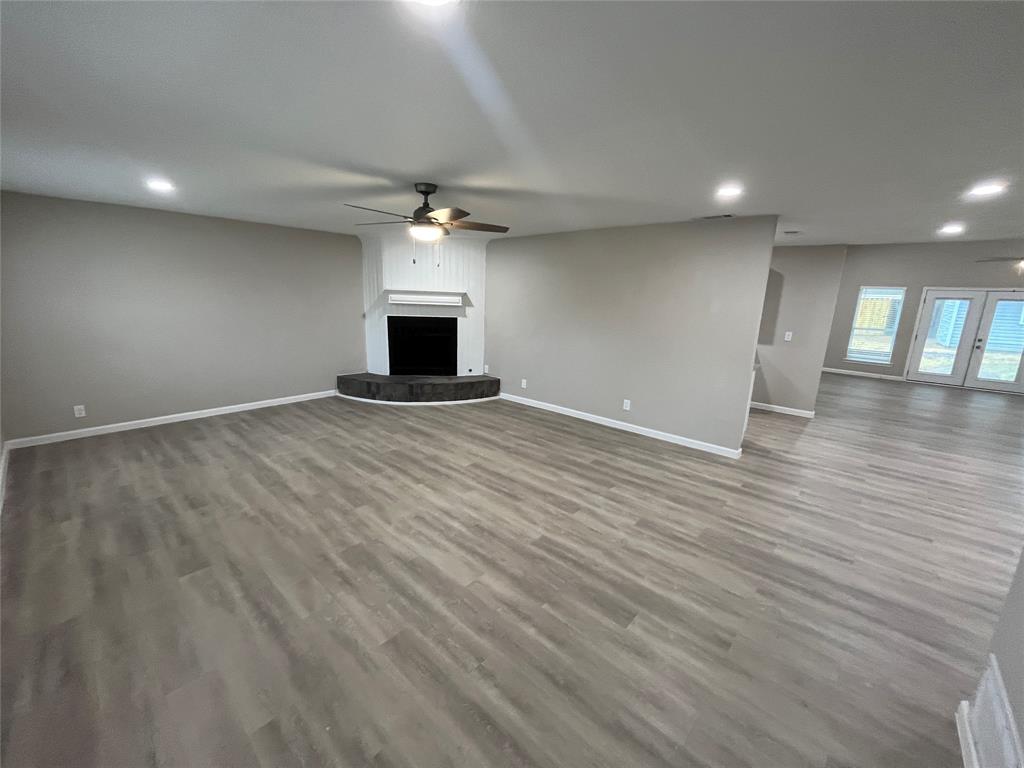 Spacious living area featuring wood-finish flooring, recessed lighting, and a corner fireplace with a dark stone hearth