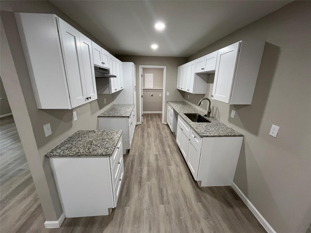 Contemporary galley kitchen featuring white shaker-style cabinetry, granite-style countertops, a double basin sink with a high-arch faucet, and wood-finish flooring