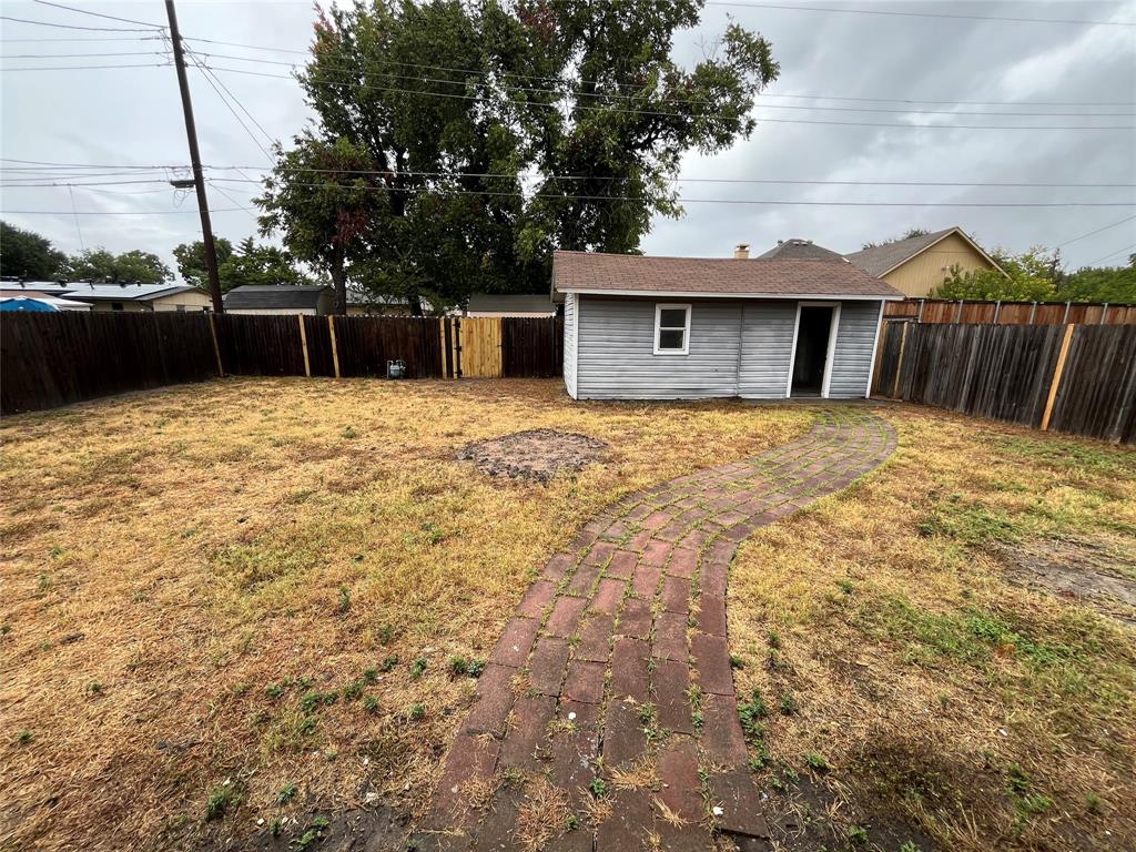 Fenced backyard featuring a brick pathway and a detached storage shed