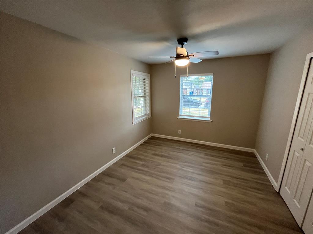 Wood-finish flooring, neutral wall tones, two windows with blinds, a ceiling fan with integrated lighting, and a bi-fold closet door