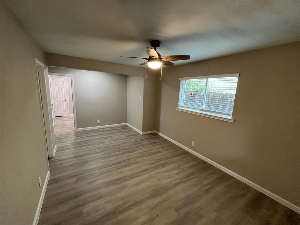 Wood-finish flooring, ceiling fan with integrated lighting, window with blinds, neutral wall tones, and white trim