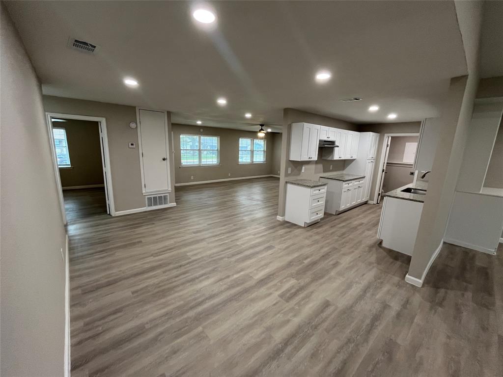 Open-concept living space with recessed lighting, wood-finish flooring, white cabinetry, and granite countertops