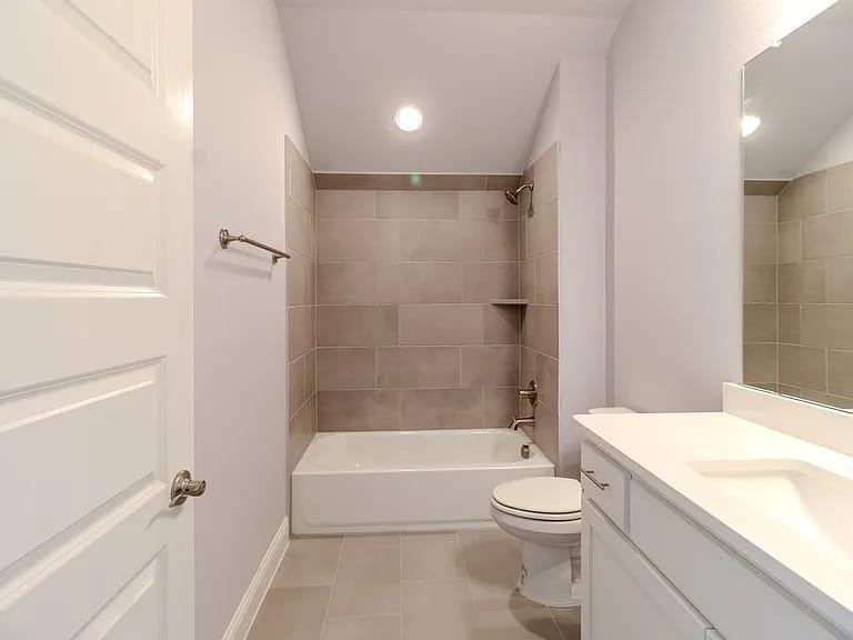 Bathroom featuring a white vanity with integrated sink, a rectangular mirror, a bathtub with tiled surround, and a built-in shower niche