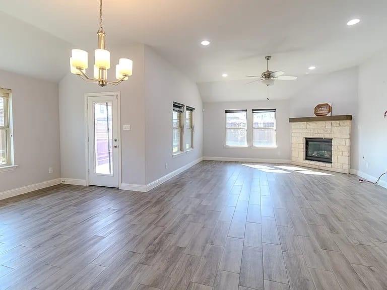 Spacious room featuring vaulted ceilings, recessed lighting, wood-finish flooring, a stone fireplace with a wood mantle, and multiple windows