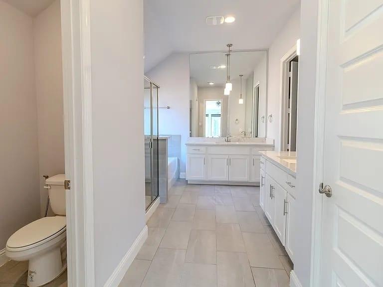 Dual vanity with white cabinetry and integrated sinks, full-length mirror, glass-enclosed shower, and a white soaking tub