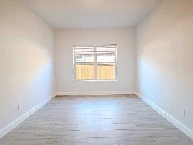 White walls with a window featuring blinds, wood-finish flooring, and white trim