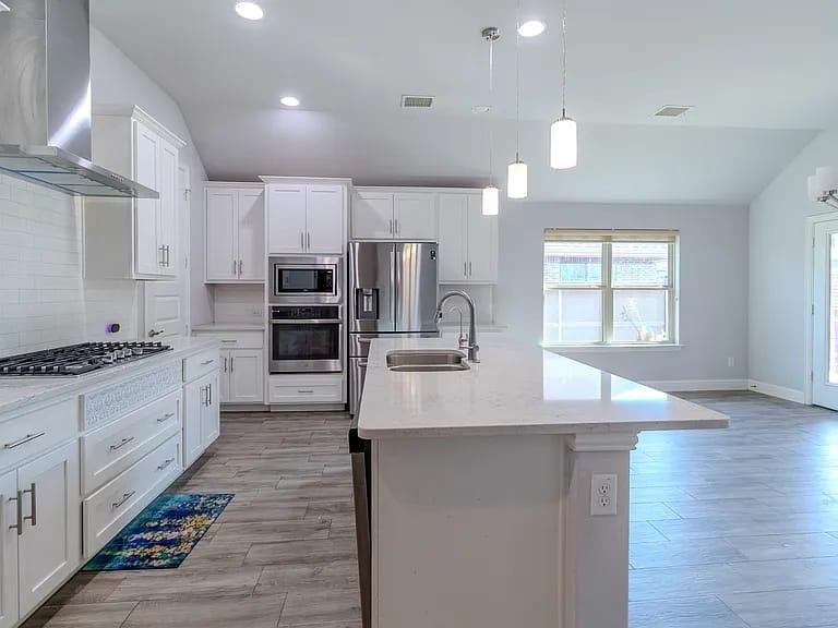 Kitchen featuring white cabinetry, stainless steel appliances, a large center island with a sink, wood-finish flooring, and recessed lighting