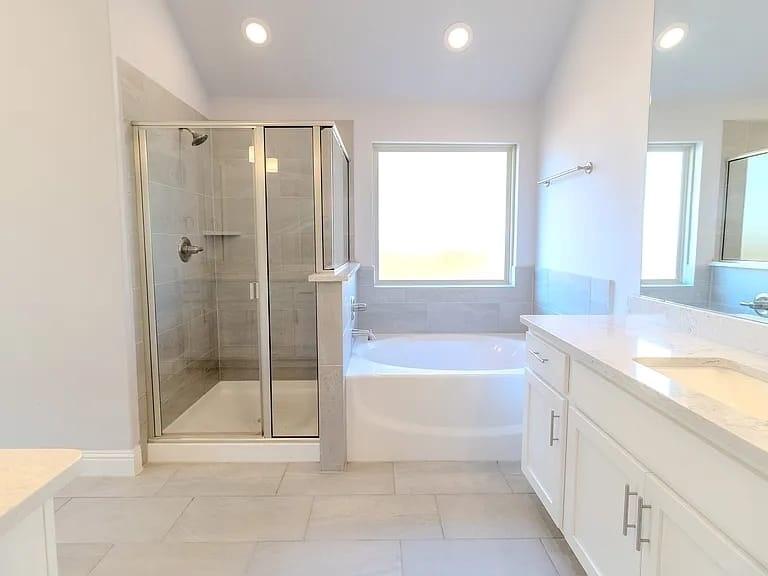 Bathroom featuring a glass-enclosed shower, a built-in tub with tile surround, a double vanity with an undermount sink, a large mirror, and recessed lighting