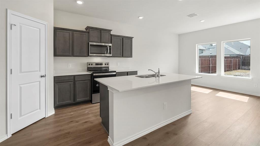 Open-concept kitchen featuring dark wood cabinetry, stainless steel appliances, a white tile backsplash, and a central island with an undermount sink