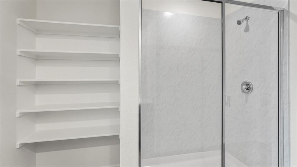 Built-in shelving unit with multiple white shelves paired with a shower enclosure featuring a glass door, white surround, and chrome fixtures