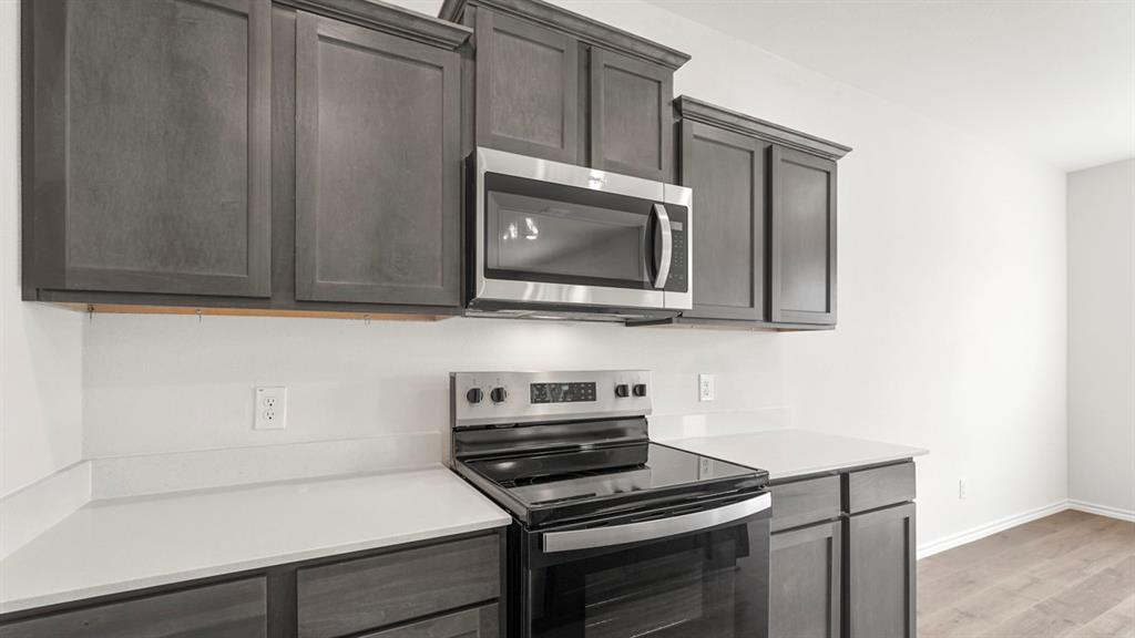 Kitchen featuring dark wood-finish cabinetry, light countertops, white backsplash, stainless steel microwave, and electric range