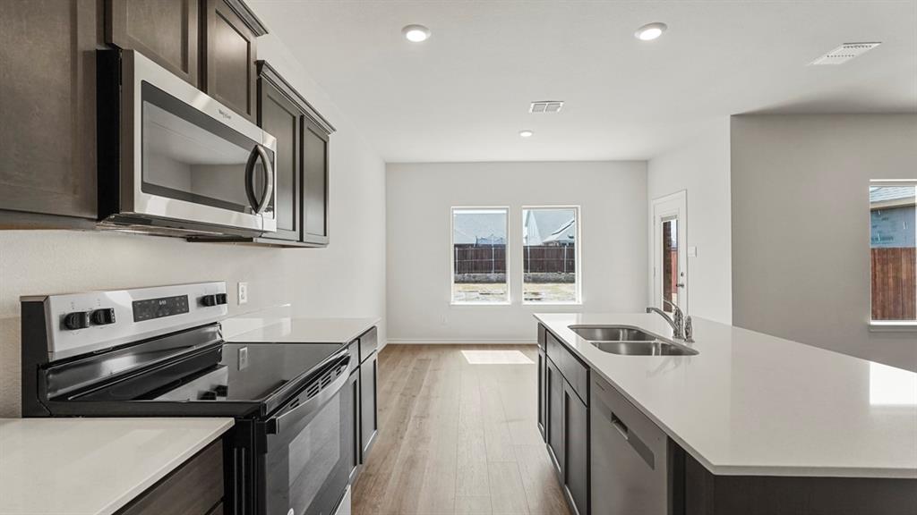 Contemporary kitchen featuring dark cabinetry, stainless steel appliances, light countertops, wood-finish flooring, and recessed lighting
