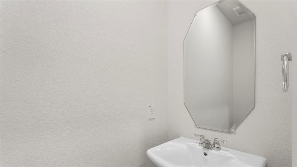 Pedestal sink with chrome faucet, complemented by a frameless octagonal mirror and a wall-mounted towel ring