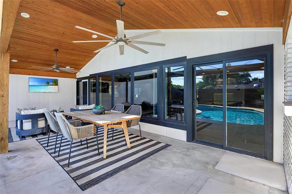 One of two covered patio featuring a vaulted wood ceiling, ceiling fans, outdoor dining and lounge areas, and direct access to the pool and two sliding doors to the main living spaces.