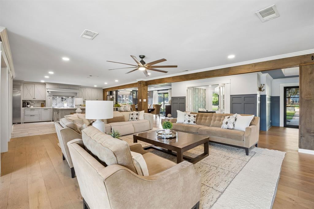 Spacious living room featuring wood floors, decorative wainscoting and exposed wood beams, with an open layout connecting to the kitchen, dining room and home office.