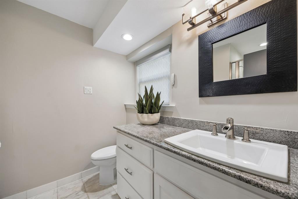 Secondary ensuite bathroom featuring a granite countertop, white cabinetry, decorative mirror, free standing shower and neutral finishes.