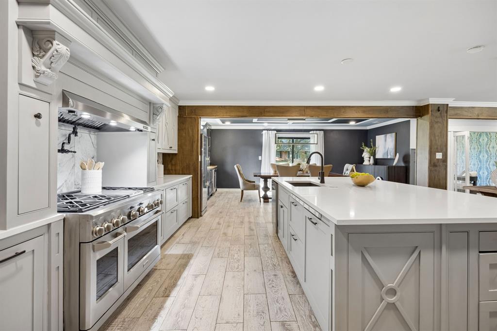 Additional kitchen view showcasing the professional-style range with double ovens, custom vent hood, oversized island and open layout connecting to the dining room.