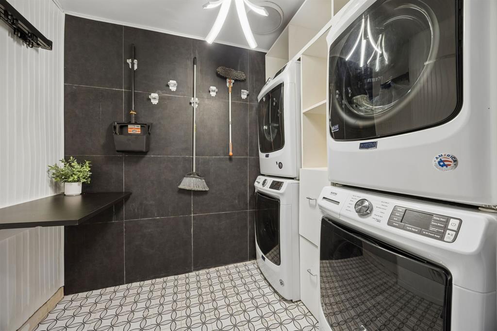 Well-appointed laundry room featuring two stacked washer and dryer sets, built-in storage, a folding counter and decorative tile flooring.