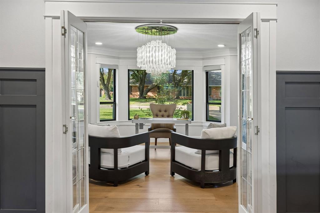 French doors open to the beautifully appointed home office, featuring a wall of windows, wood floors and a statement chandelier.
