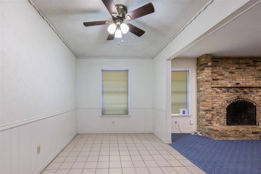 Tile flooring, white wall paneling, brick fireplace, and a ceiling fan with integrated lighting