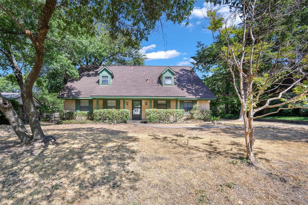 Brick exterior with green trim, dormer windows, covered front entry, and mature trees