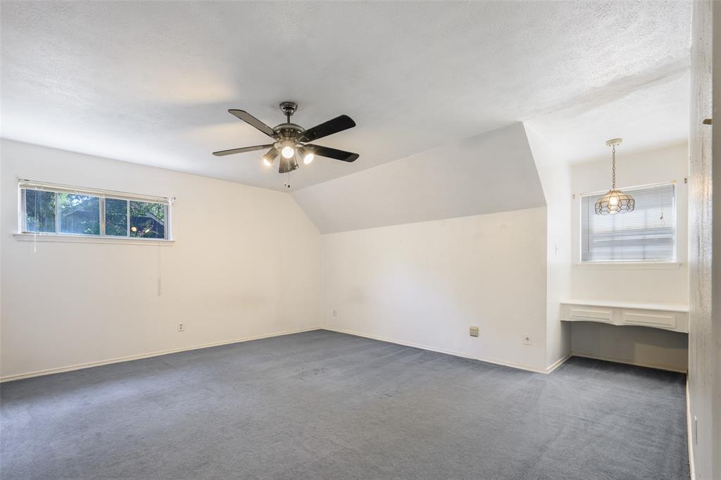 Expansive room featuring sloped ceilings, a ceiling fan with integrated lighting, a built-in desk, and a decorative pendant light fixture