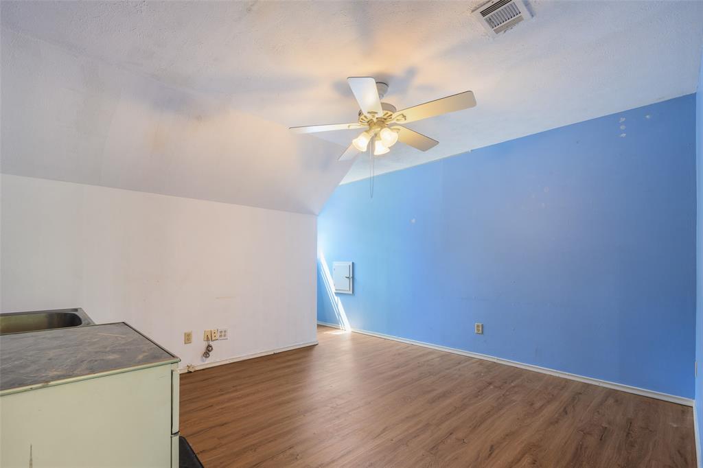 Sloped ceiling with an integrated ceiling fan, wood-finish flooring, and a compact utility sink