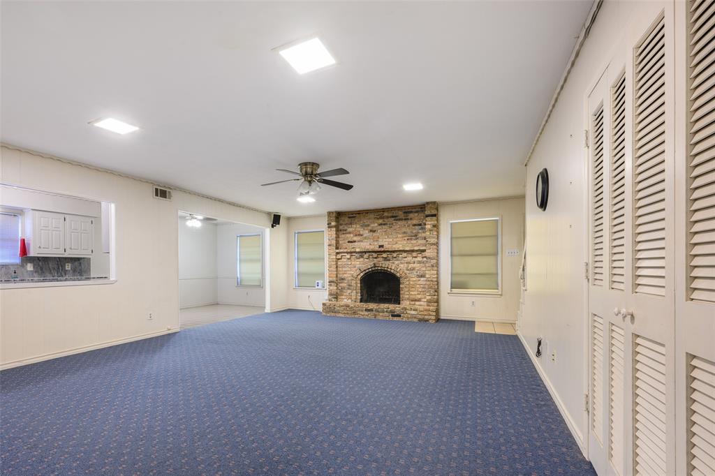 Spacious room with blue patterned carpeting, a stone-clad fireplace, and white louvered bifold doors