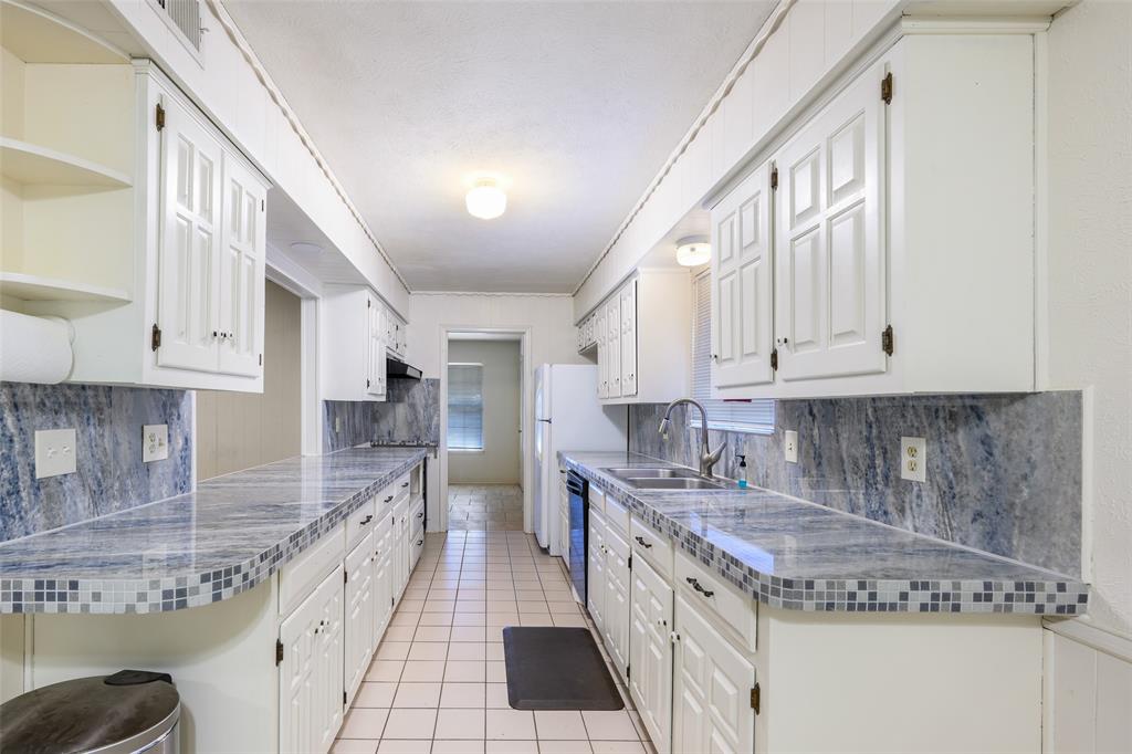White cabinetry with dark hardware, stone-look countertops with tile trim, ceramic tile flooring, and integrated dual basin sink