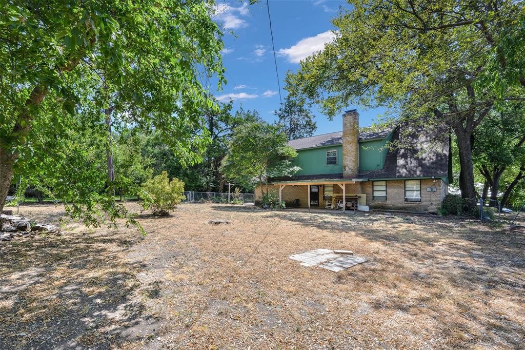 Expansive backyard with mature trees, a covered patio, and a prominent brick chimney