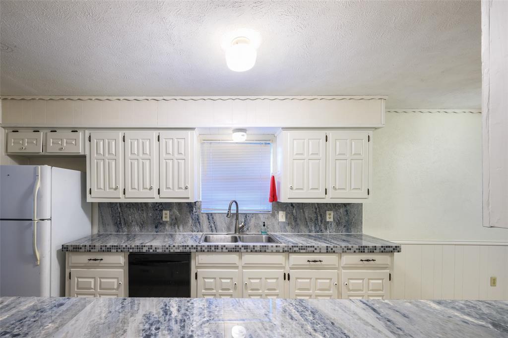 White cabinetry with dark hardware, dual basin sink with gooseneck faucet, black dishwasher, and stone-look countertops with tile trim