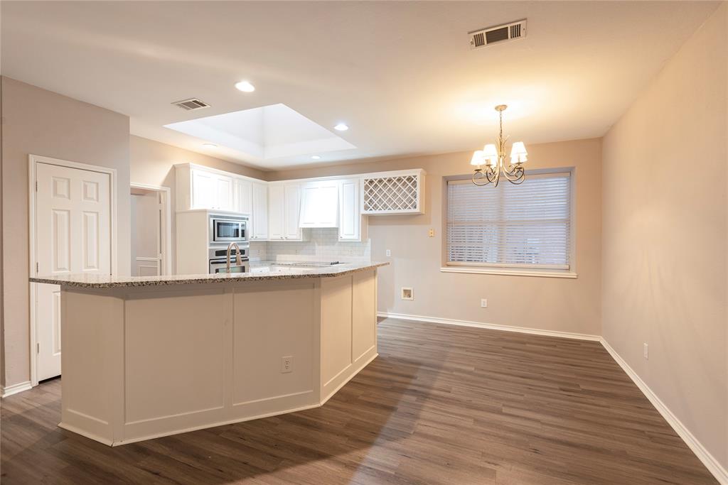 Kitchen featuring light stone countertops, decorative light fixtures, white cabinetry, and a kitchen island with sink
