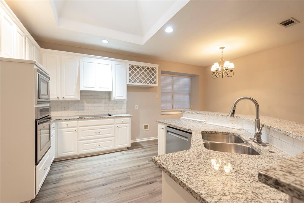 Kitchen with pendant lighting, white cabinets, sink, light stone counters, and stainless steel appliances