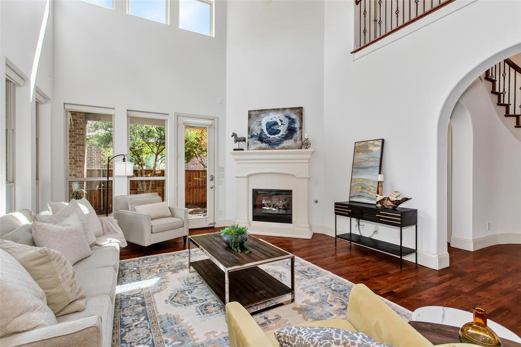 Two-story living room featuring rich wood flooring, a fireplace with a mantel, tall windows, and an arched entryway