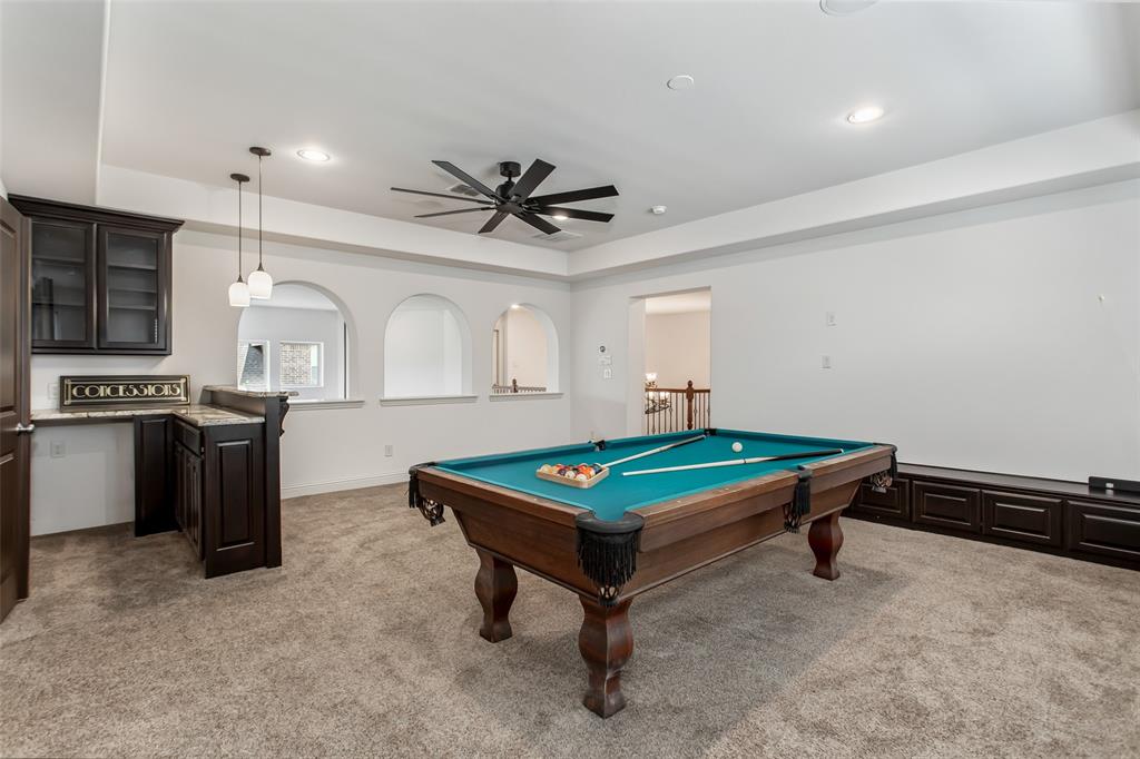 Spacious recreation room featuring a built-in wet bar with dark wood cabinetry, granite-style countertop, and pendant lighting