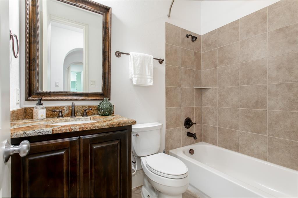 Bathroom featuring a built-in vanity with a stone countertop, an integrated sink, a framed mirror, and a bathtub with a tiled surround
