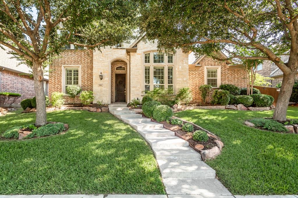 Brick and stone facade, arched entryway, bay window, concrete walkway, and landscaped garden beds