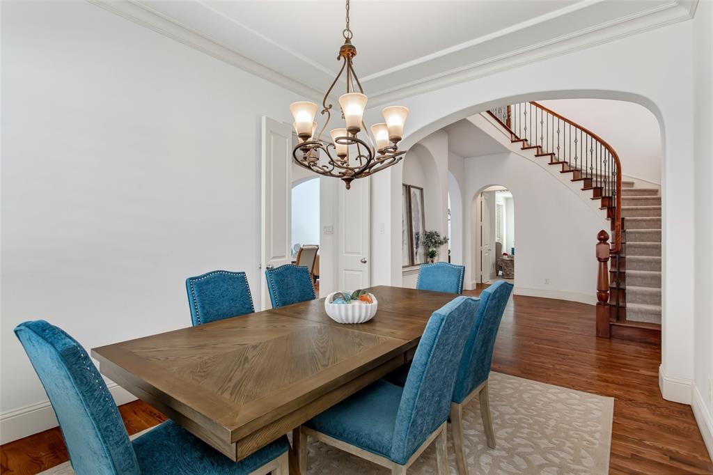 Arched entryway leading to a staircase with wood newel post and balusters, featuring hardwood flooring and a chandelier
