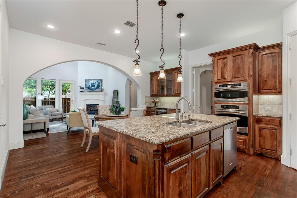 Gourmet kitchen featuring a central island with a double basin sink and granite countertop, rich wood-finish cabinetry, stainless steel double ovens, and recessed lighting