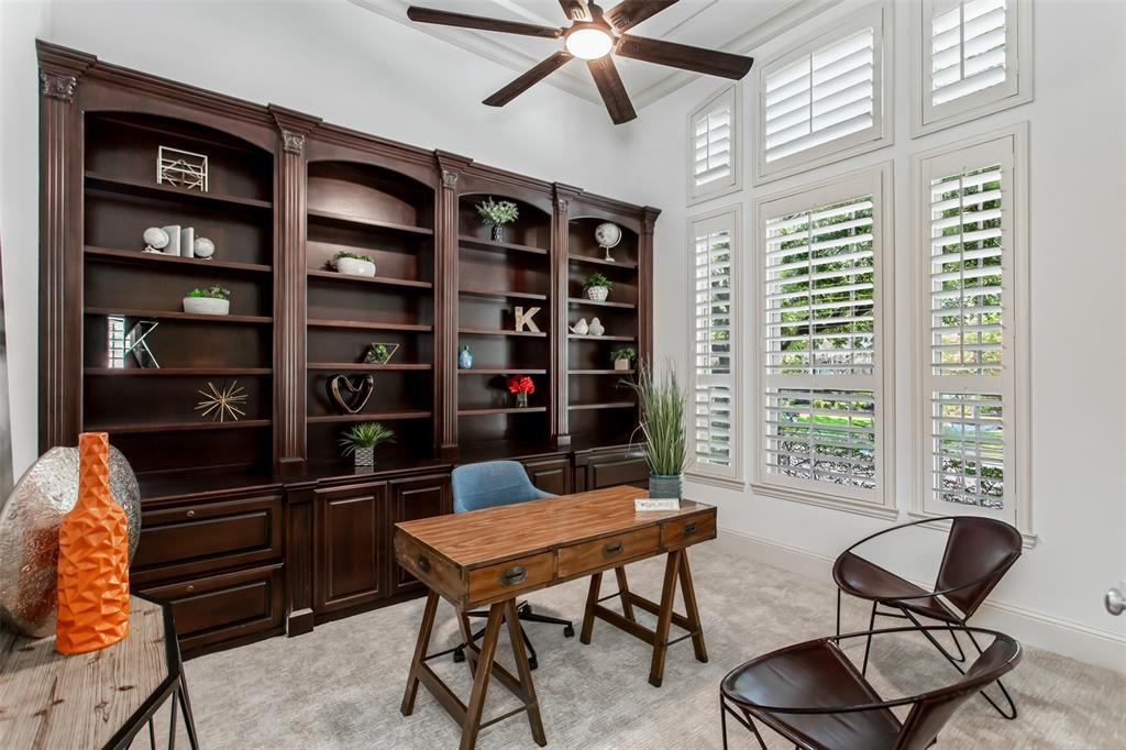 Built-in cabinetry with dark wood finish, multiple window panels with plantation shutters, ceiling fan with integrated lighting, and vaulted ceiling