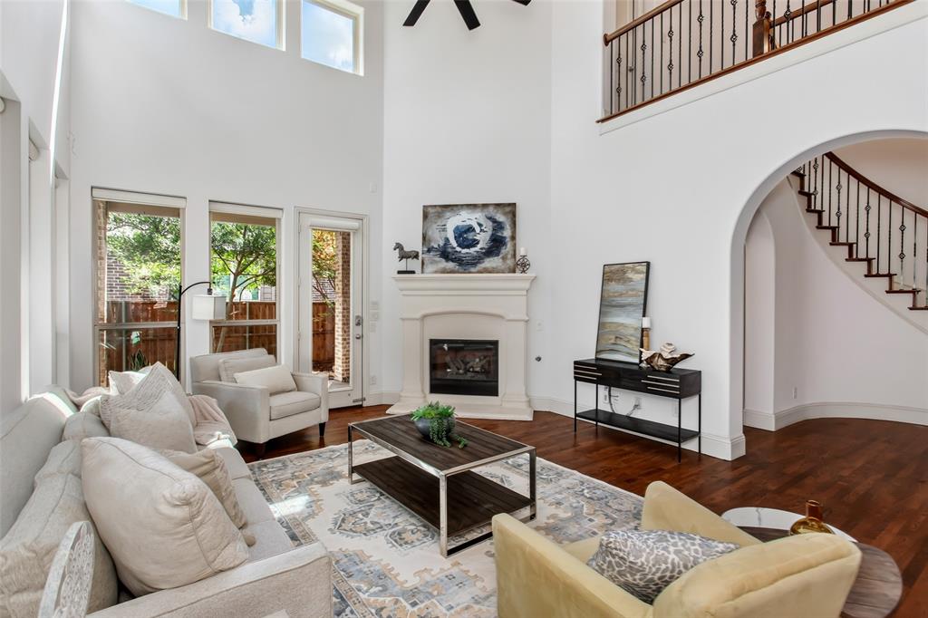 Two-story living area featuring a fireplace with a stone surround, rich wood-finish flooring, a wrought iron staircase, high ceilings, and multiple windows