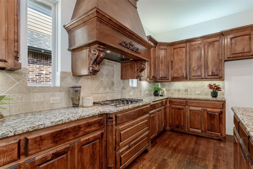 Wood cabinetry, granite countertops, decorative range hood, gas cooktop, and tile backsplash